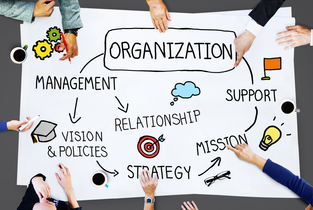 Hands collaborating on an organization strategy chart with keywords like management, mission, vision, and support.