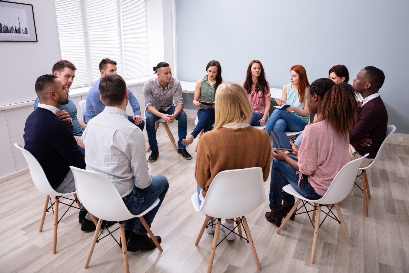 A social worker holds a group counselling session to multiple adults who are sitting in a circle on chairs. Sparkrock's ERP features can help free up time for practitioners to focus on what they do best - help their patients.