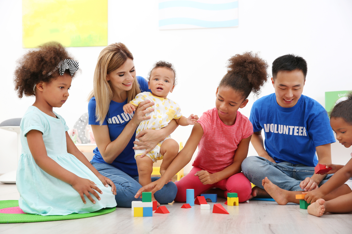 Two adult volunteers take care of three children while they are playing. Utilizing Sparkrock 365 ERP, the nonprofit efficiently manages child care duties with volunteers. This empowers them to spend more time directly assisting and working with the kids, fulfilling their mission effectively.