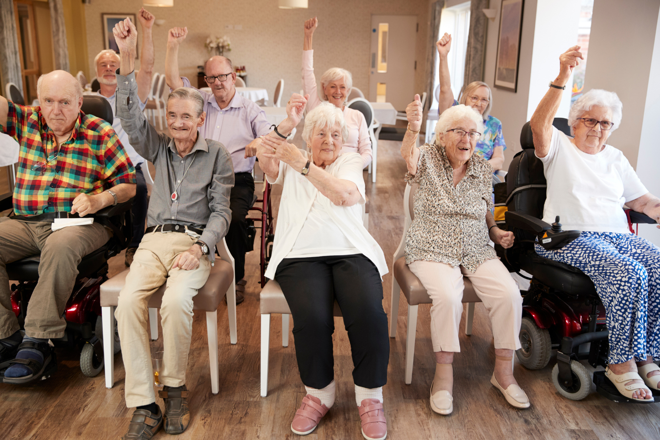 A group of older adults have fun and throw their hands up in at air during a session at their long term care home.