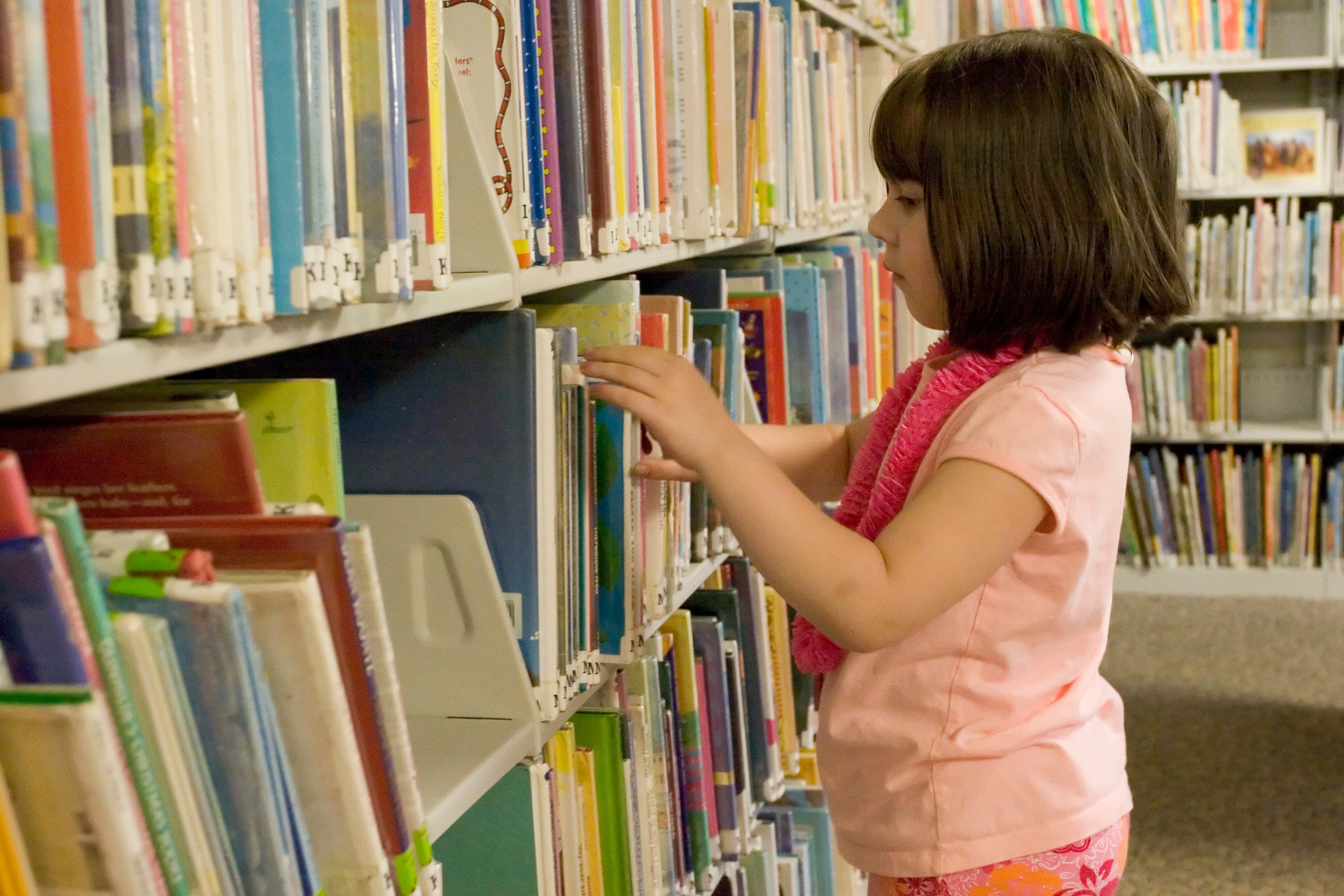 A little girl looking at books in a library. Arts and culture organizations using Sparkrock 365 ERP are more efficient, allowing them to focus on sharing the value and creativity of the arts with ample time and resources.