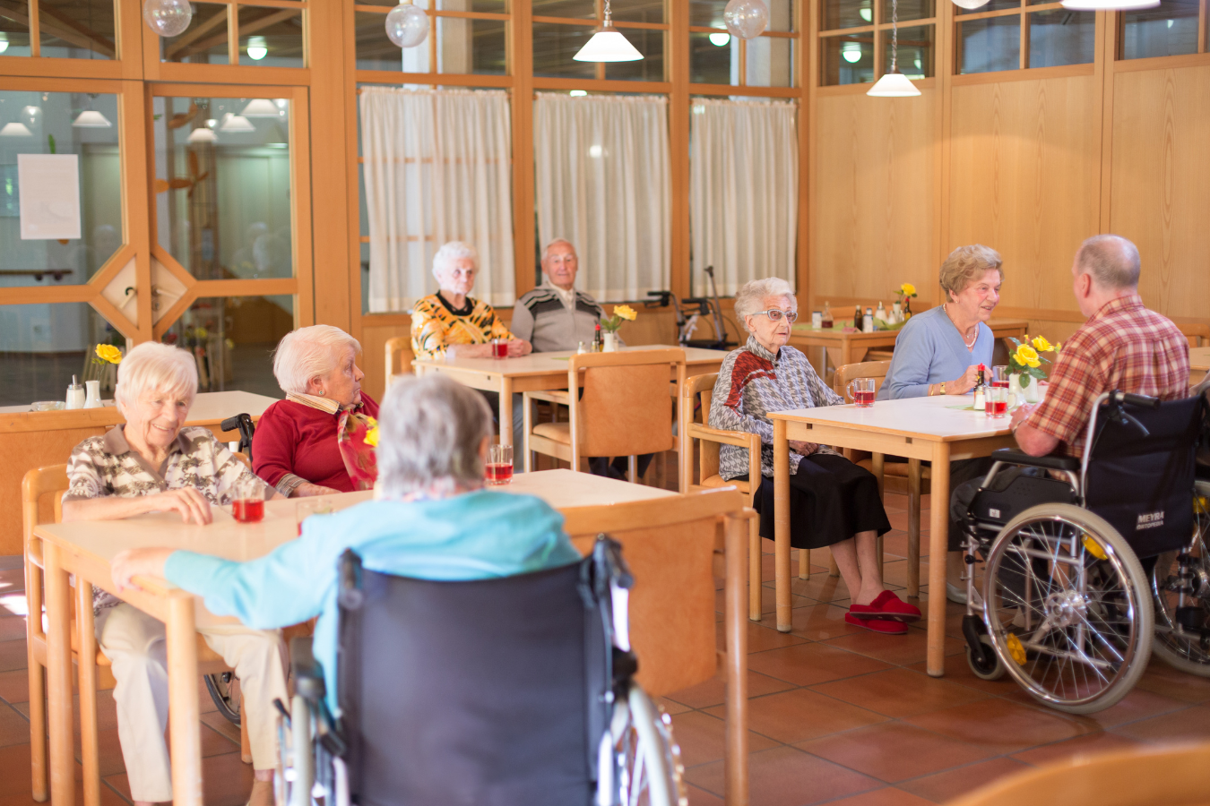 Residents in a long-term care home, residential care facility wait for dinner together in the dining room.