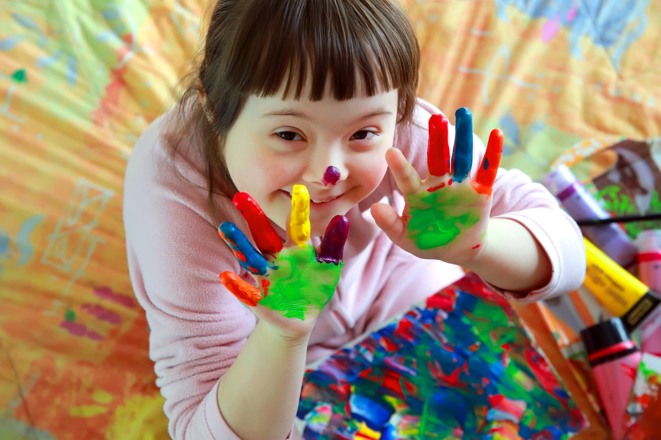 A young girl with Down Syndrome plays with rainbow paint and is smiling. Sparkrock 365, an ERP system for Human Services organizations, helps administrators eliminate burdensome tasks and focus on what they do best - helping people.