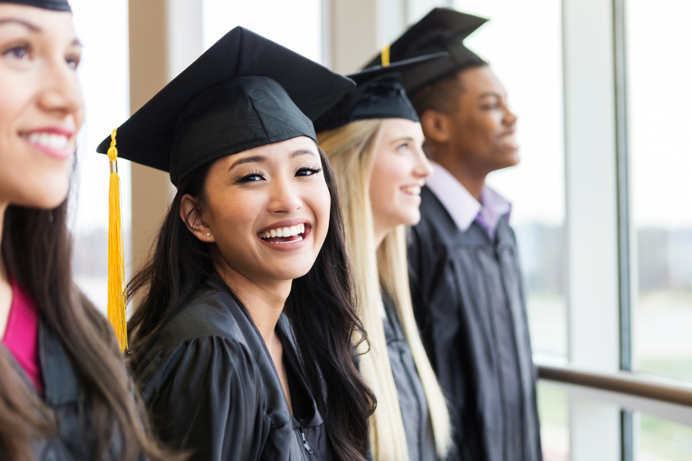 A group of high school students stand in their graduation gowns, with one girl smiling towards the camera. ERP solutions help K-12 organizations manage their finances, human resources, and payroll, to help schools focus on the success of their students.
