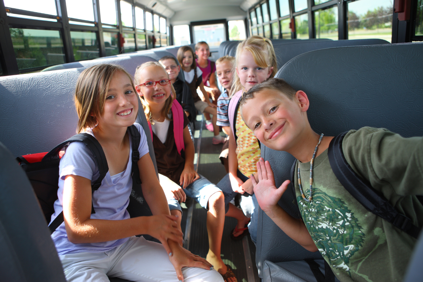 8 K-12 school kids sitting on a bus and waving at the camera. K12 ERP software like Sparkrock 365 helps administrators focus on long-term success for their school districts.