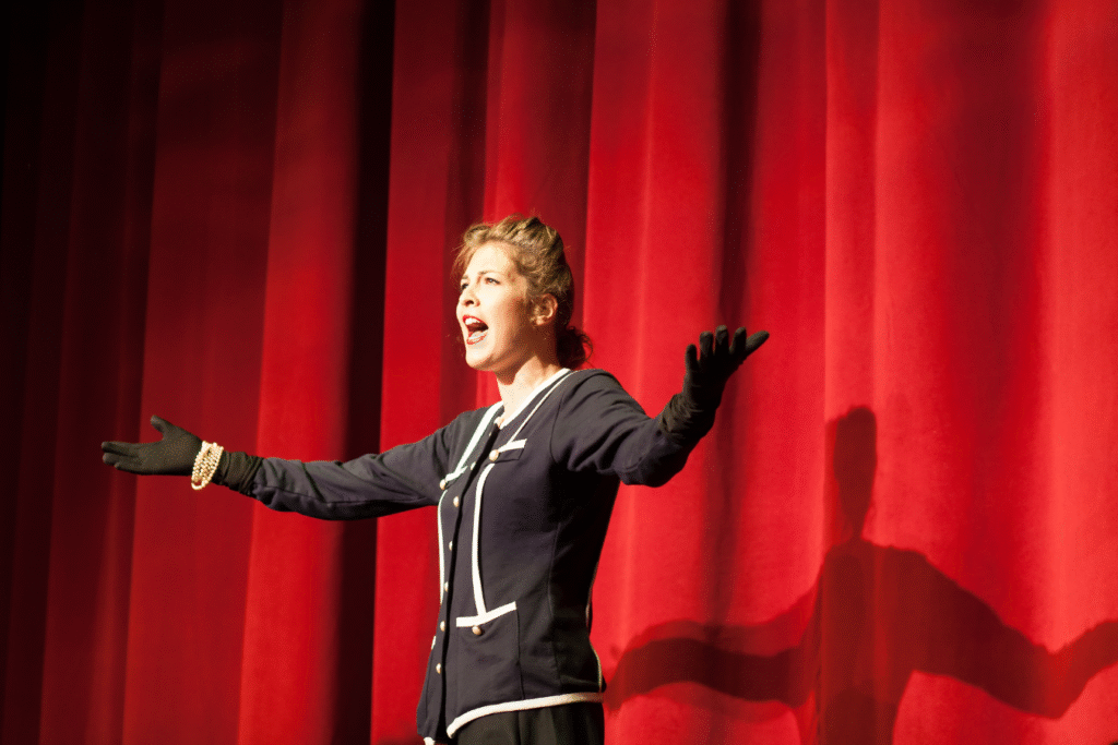 Performer on stage in front of red curtains, arms outstretched — representing the National Arts Centre’s thoughtful, collaborative ERP evaluation process that led to choosing Sparkrock with confidence.