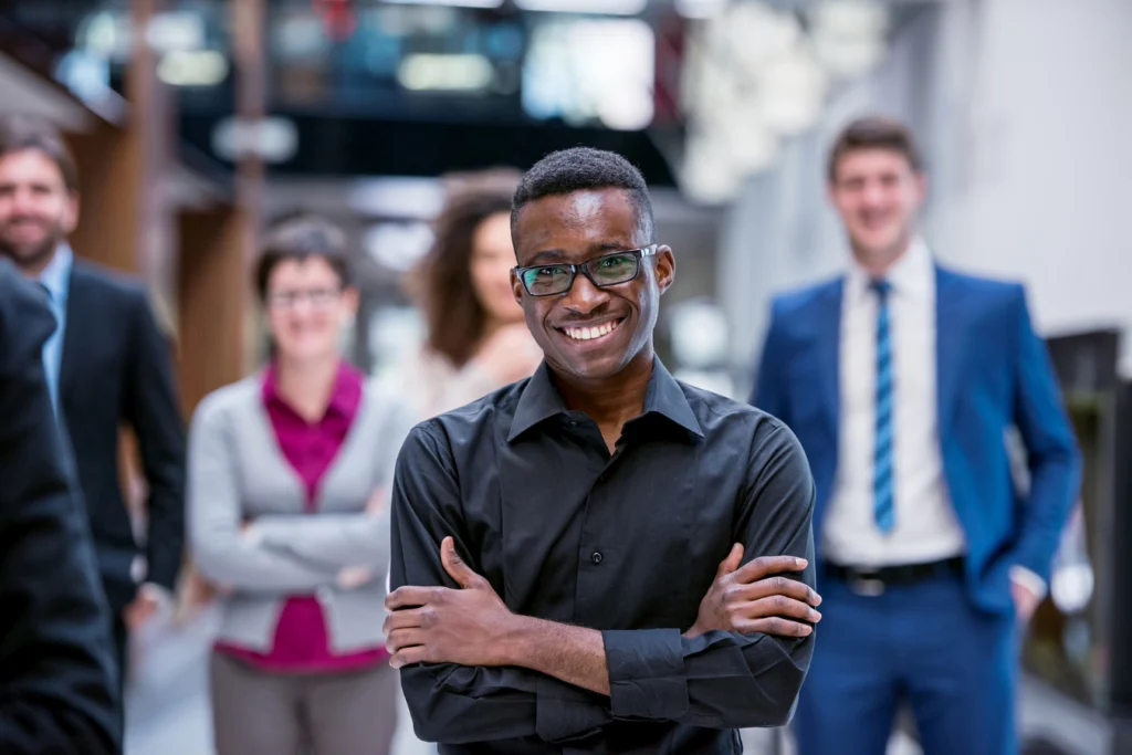 Smiling nonprofit executive standing with arms crossed, supported by team in the background, symbolizing strong leadership during ERP change.
