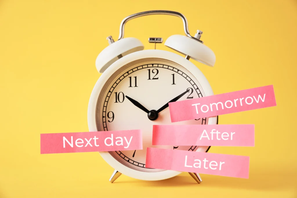 White alarm clock on a yellow background with pink paper labels reading “Tomorrow,” “Next day,” “After,” and “Later,” symbolizing nonprofit delays in digital change.