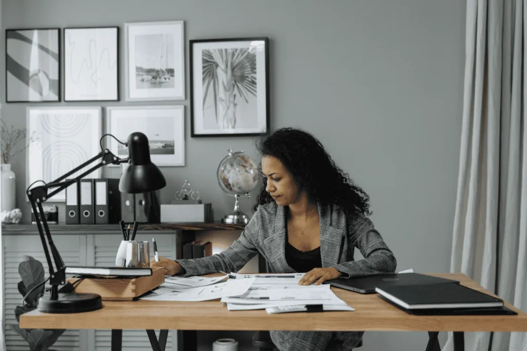 Female school administrator sitting at her desk reviewing payroll documents and financial reports, representing the complexity of K-12 payroll management.