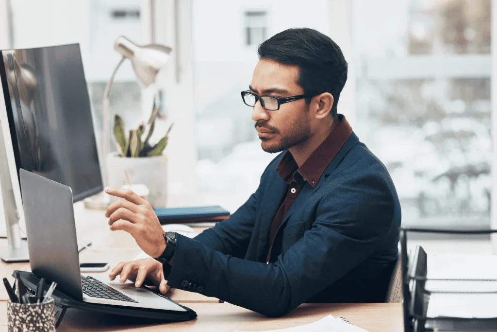Male administrator working at a desk, focused on his laptop, reviewing data and managing payroll calculations in an office setting.