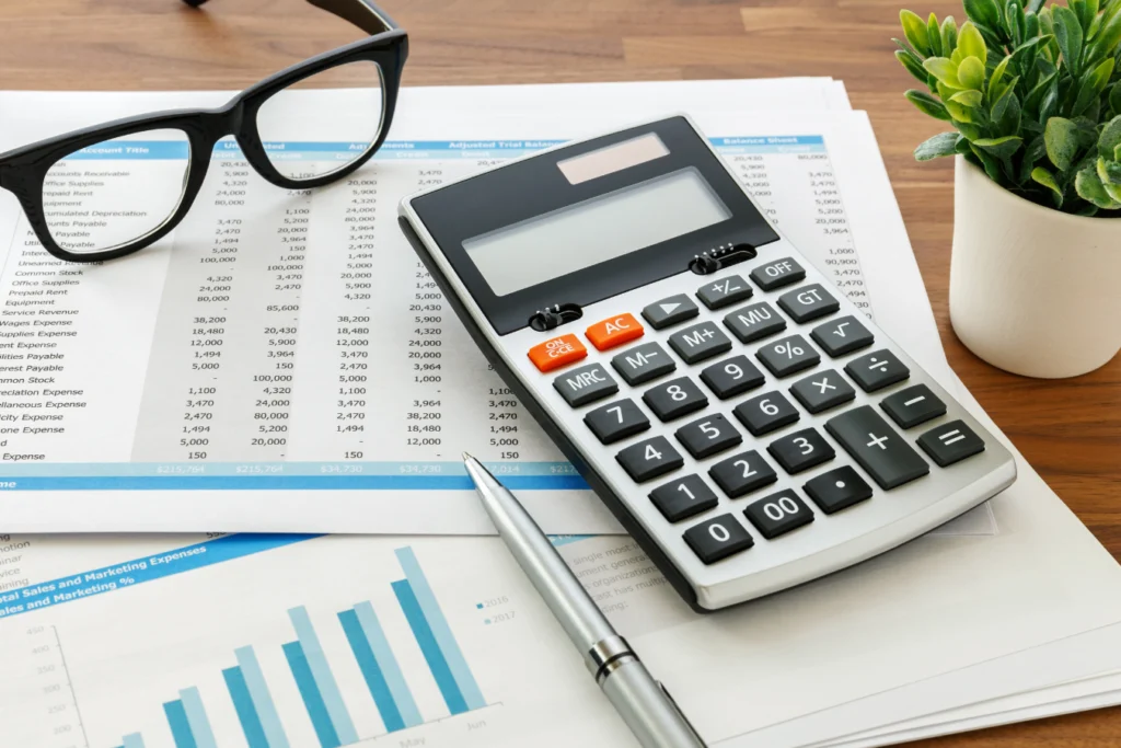 Calculator, financial reports, and glasses on a desk representing nonprofit ERP reporting and the shift from complex GL accounts to dimensional accounting
