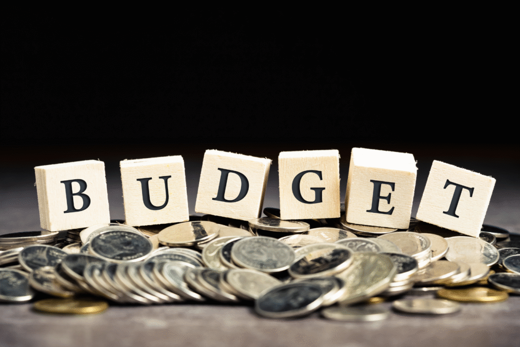 Wooden letter blocks spelling "Budget" placed on a pile of coins, representing the granular cost detail behind every nonprofit budget line