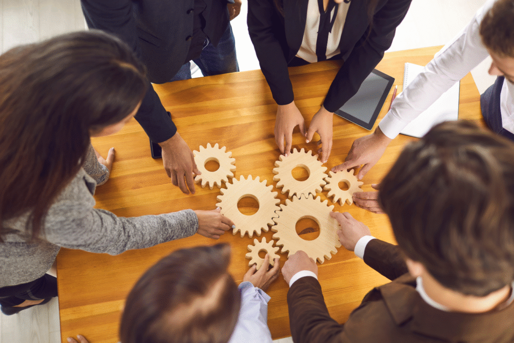 Group of professionals fitting interlocking wooden gears together on a table, representing how connected HR and finance systems work together as one