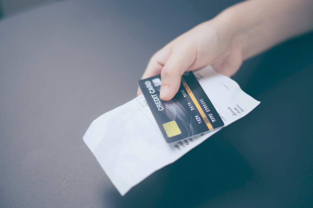 Hand holding a credit card and receipt, representing the manual expense tracking and reconciliation process nonprofits deal with monthly