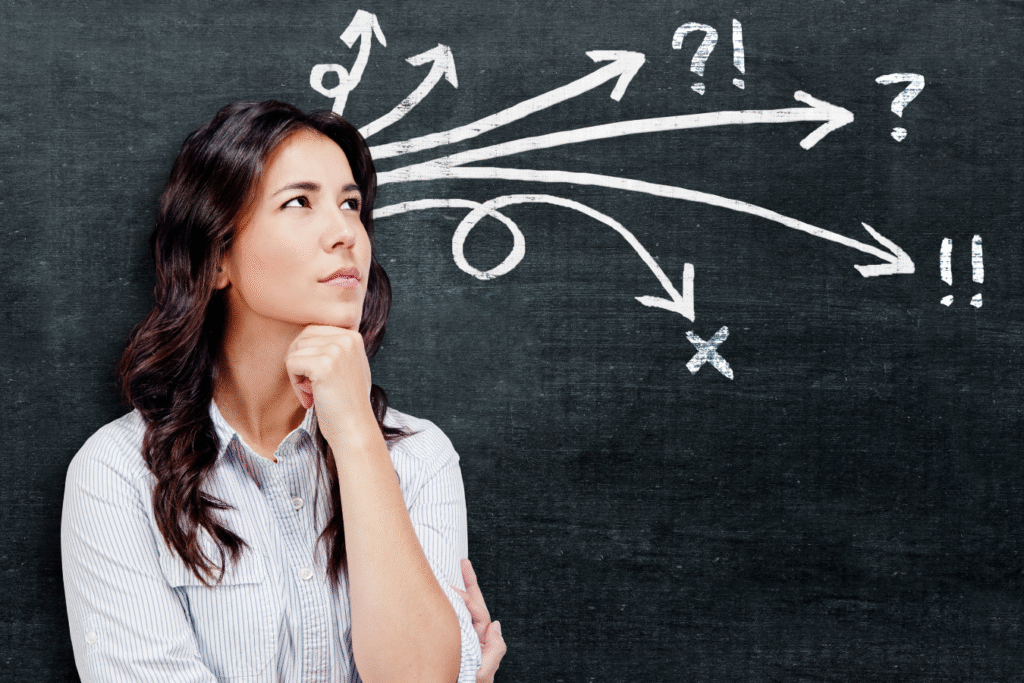 Woman thinking in front of a chalkboard with multiple arrows and question marks, representing the build, buy, or bolt-on decision nonprofits face when evaluating a new ERP system