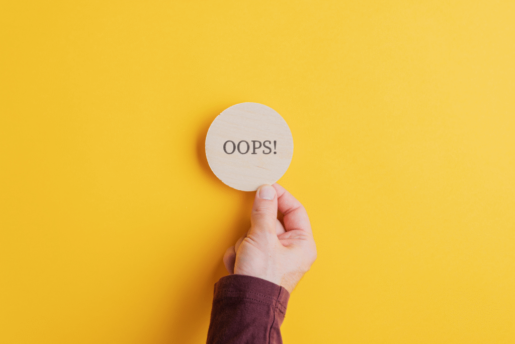 "Hand holding a wooden sign that says 'Oops!' against a yellow background, representing common activity fund management mistakes in schools."